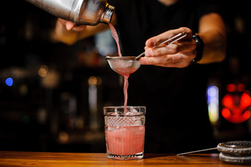 barman poured an alcoholic cocktail from the shaker into a crystal glass