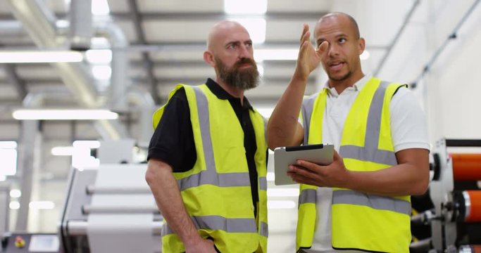 4k, Two managers standing inside a printing and packaging plant with a digital touchscreen tablet. Slow motion.