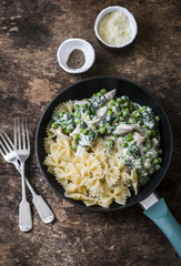 One pot creamy chicken spinach and green peas farfalle pasta in the pan on brown wooden background, top view
