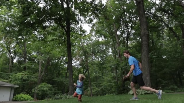 Cheerful father chasing son while playing baseball at yard
