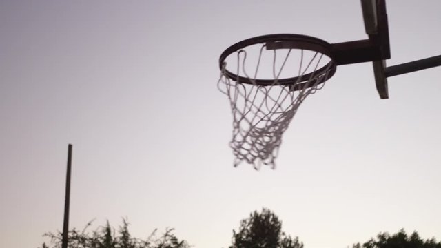 Handheld shot of man playing with friend dunking basketball in hoop against sky during sunset