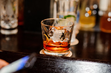 half-empty glass with whiskey and ice stands on a brown wooden bar counter