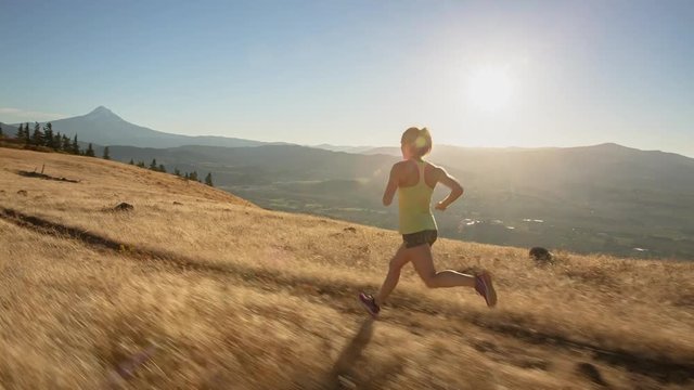Handheld shot of young woman jogging on trail against mountains during sunny day