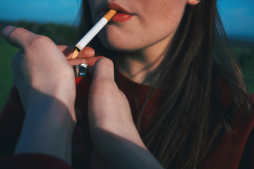 The girl is smoking a cigarette. Female hands hold a lighter.