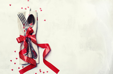 Festive table setting for Valentines Day, set of cutlery, red ribbon and sweet hearts, gray...