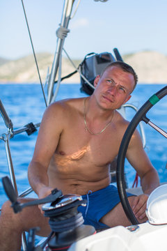 Young man at the helm of a sailing yacht boat.