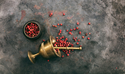 Pink peppercorns and a bronze mortar on metal rusty background, top view, copy space
