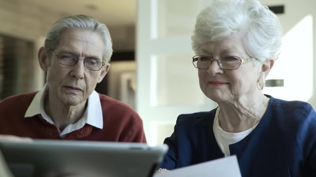 Dolly shot of happy senior couple looking at tablet computer with financial advisor in office