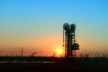 Working oil derrick in field under the setting sun