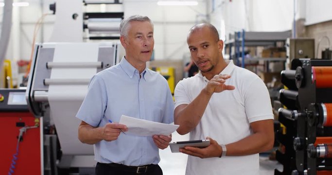 4k, Two managers standing inside a printing and packaging plant with a digital touchscreen tablet. Slow motion.
