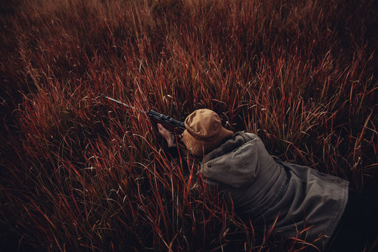Hunter laying in high grass with rifle aiming on prey
