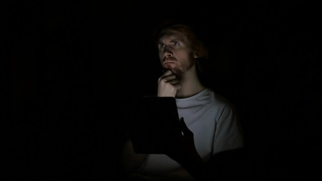 Redhead Man Thinking and Working on Tablet at Night