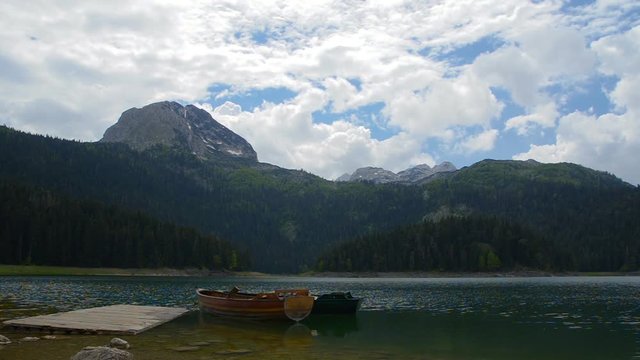 Timelapse shot of a mountain lake in Montenegro. Summer period with light wind that gently waves the surface of the waters of the Black Lake below the Durmitor Mountain. On a wooden dock, moored boats