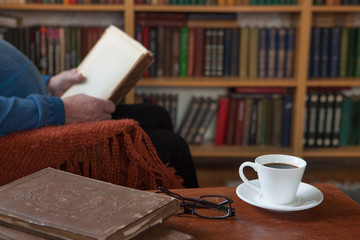Sweet moments of relaxation with books and a cup of coffee. Vintage books, glasses, chair, library, man