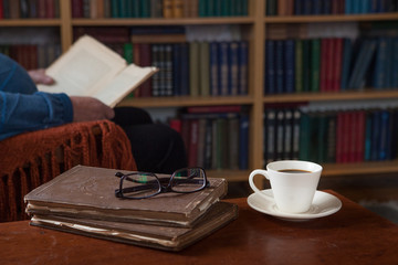 Sweet moments of relaxation with books and a cup of coffee. Vintage books, glasses, chair, library, man