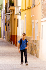 Little pretty boy walking in european city street with his backpack.