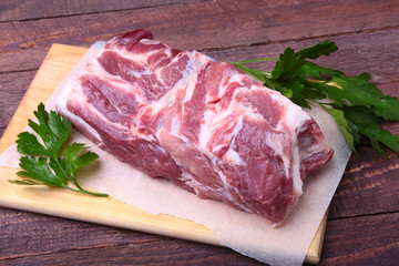 Raw pork neck chop meat with parsley herb leaves on a stone background. Ready for cooking.