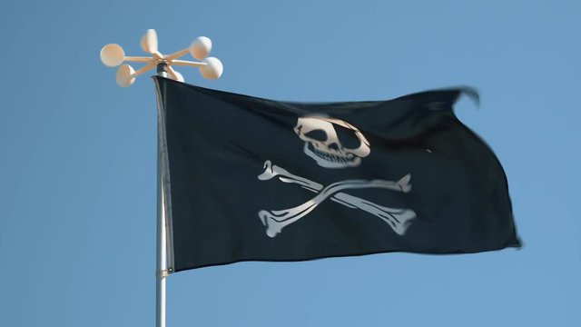 Pirate flag with symbols of black color fluttering in the wind against the blue sky background close-up on the beach