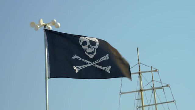 Slide of pirate flag with symbols of black color fluttering in the wind against the blue sky background close-up on the beach