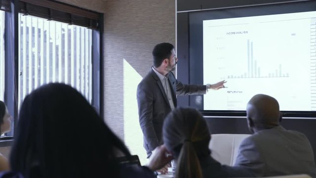Dolly shot of businessman giving presentation to colleagues in meeting at board room