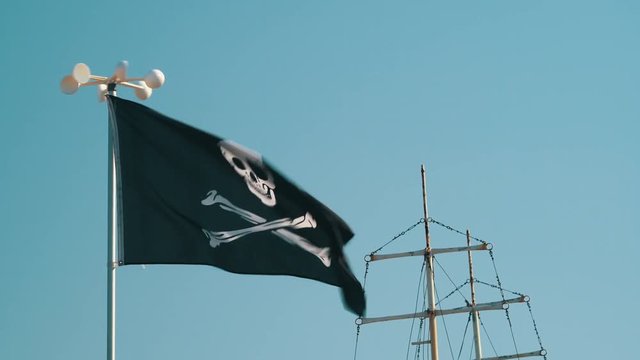 Pirate flag with symbols of black color fluttering in the wind against the blue sky background close-up on the beach