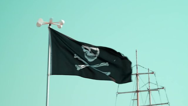 Slide of pirate flag with symbols of black color fluttering in the wind against the blue sky background close-up on the beach