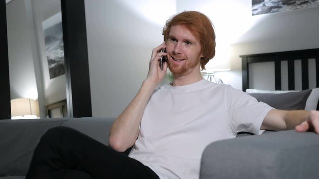 Redhead Man Talking on Phone, Sitting on Couch in Bedroom