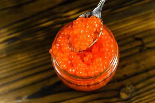 Red caviar in a spoon above the glass jar