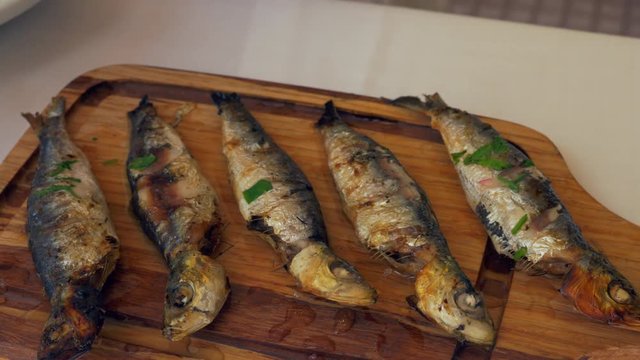 Close-up Shot Of Woman Squeezing Lemon Juice On Grilled Sardines Served On Wooden Board