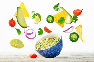 Guacamole with flying corn chips and ingredients to prepare it