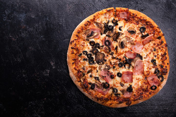 Top view of fresh baked pizza with ham, olives and mushrooms on dark wooden background with copy space available