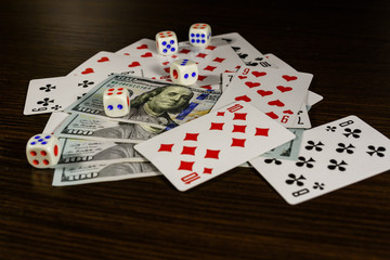 Playing cards, dice and one hundred dollar bills on a dark wooden table