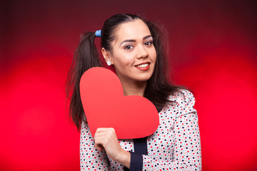 Smilng woman holding a red papper heart in hands on dark red background