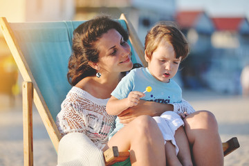 Young woman with baby sitting in chair on summer beach.