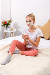 beautiful young woman with white clay facial mask with milkshake in mason jar at home