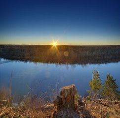 The sun at sunset illuminates the river bank.