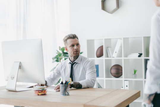 handsome young tattooed businessman looking away while working with desktop computer in office