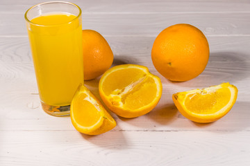 Glass of orange juice and fresh oranges on white wooden table