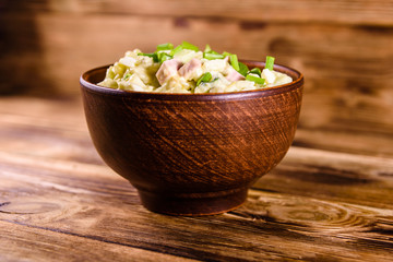 Ceramic bowl with russian traditional salad olivier on wooden table
