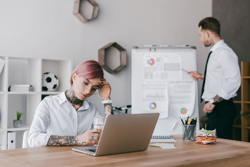 young businesswoman using laptop while businessman working with whiteboard in office