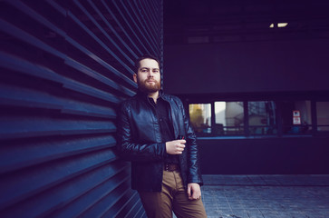 Cool man in a black leather jacket with standing against a blue background.
