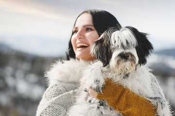 Happy woman holding her Tibetan terrier puppy in winter scenery, selective focus on dog