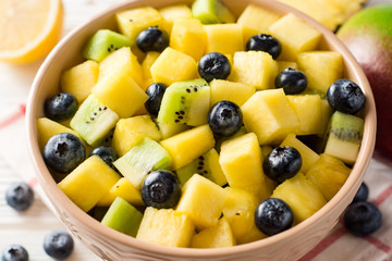 Fresh fruit salad with pineapple, mango, kiwi and blueberries on white wooden background.