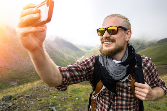 Man Traveler With Beard Makes Selfie In The Background Of A Mountain Landscape. Journey Hiking Concept