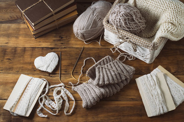Fototapeta na wymiar Light gray Knits in a basket and knitting needles, a white knitted scarf, a heart. Set with white ribbons on a wooden background. The concept of handmade. Flat lay, top view