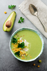 Homemade tender soup puree from avocado and corn with cream in rustic ceramic plate on gray...