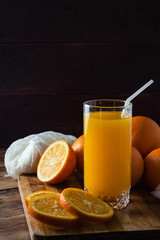 A glass of orange juice with a pipe, a cut orange, oranges on a wooden board, a dark background. Beautiful Game of Light and Shadows