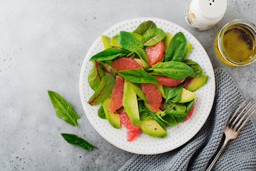Useful tasty salad of spinach, chard, avocado and grapefruit with olive oil on old concrete gray background. Selective focus. Top view. Copy space.