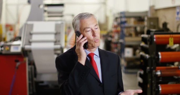 4K Serious mature businessman in factory negotiating a difficult deal over the phone. Slow motion.
