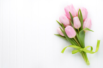 Fresh pink tulip flowers bouquet on shelf in front of wooden wall.